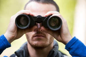 Close-up of male hiker looking through binoculars in forest