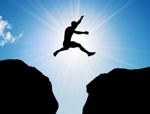 man jumpin the chasm between two rocks with sun shinning in background